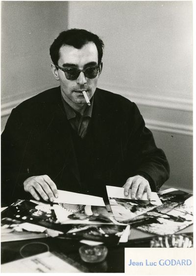 Paris: N.p., 1960. Two vintage photographs of director Jean-Luc Godard, dark sunglasses and cigarett...