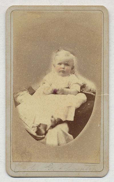 [Photograph]: Infant In White Dress sitting on a cushion, cheeks highlighted with pink, identified in pencil in lower margin as "Lzole. G. Thornton